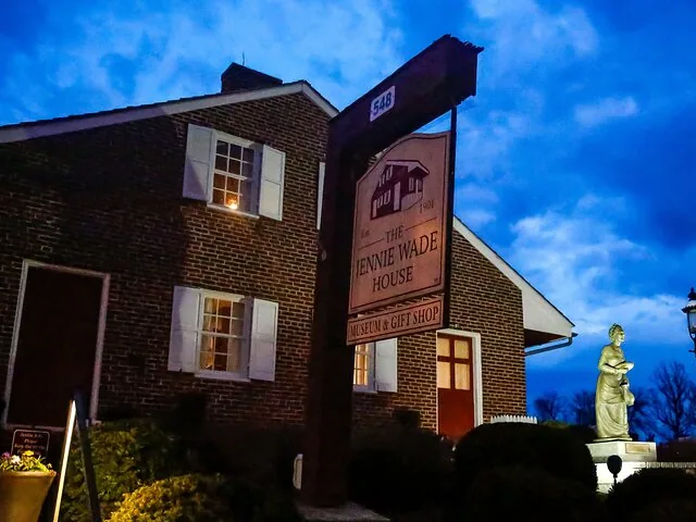 Außenansicht des Jennie Wade House in der Abenddämmerung mit beleuchtetem Schild und Statue