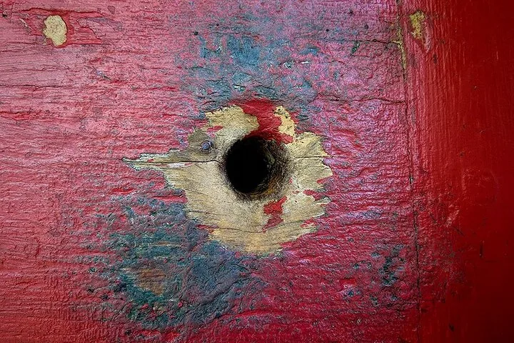 Close-up of a bullet hole in a red painted wooden door